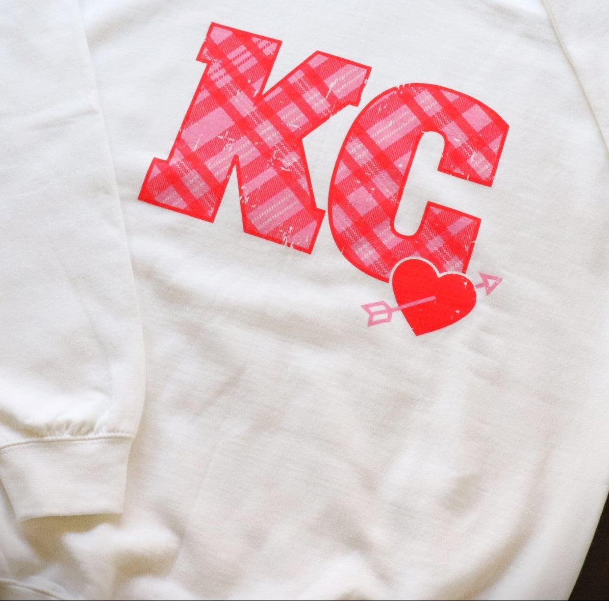 White sweatshirt with red 'KC' lettering and heart design on a gray surface